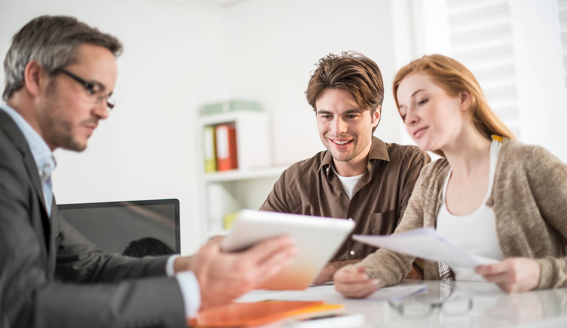 Berater präsentiert einem jungen Paar digitale Lösungen auf einem Tablet im modernen Büro.