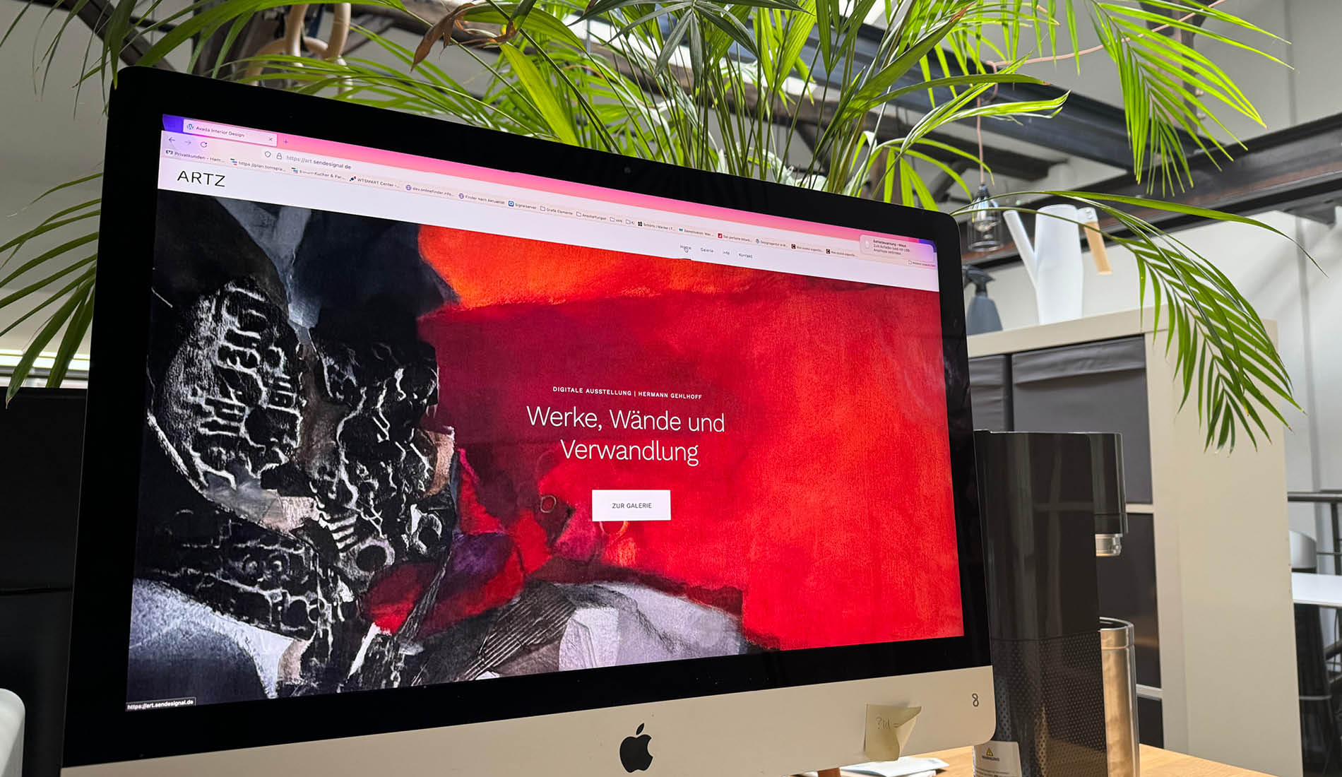 Website einer digitalen Kunstgalerie mit rotem Hintergrund auf einem iMac im modernen Büro.